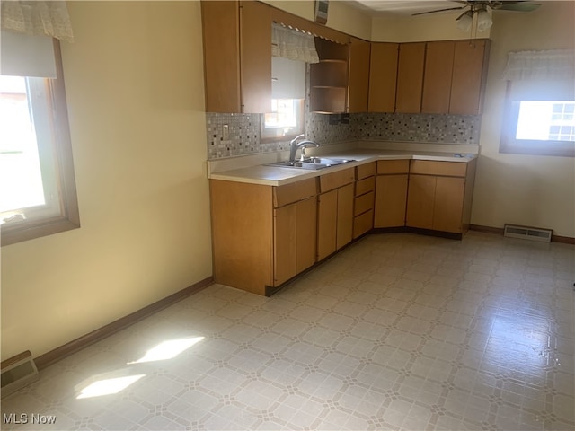 kitchen with a sink, light countertops, tasteful backsplash, baseboards, and ceiling fan