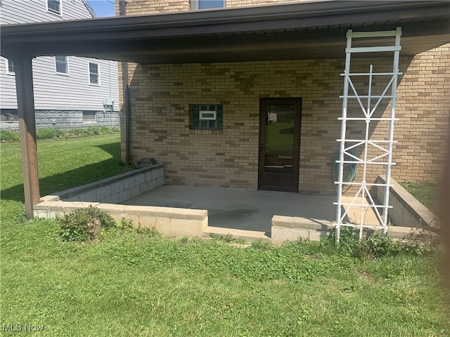 view of exterior entry with brick siding, a lawn, and a patio