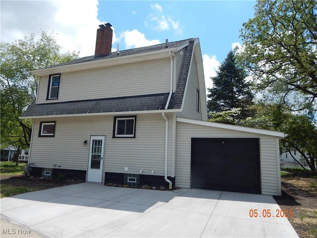 rear view of house featuring concrete driveway, a chimney, an attached garage, and roof with shingles