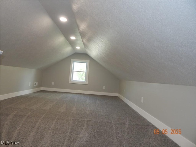 additional living space with a textured ceiling, vaulted ceiling, baseboards, recessed lighting, and dark colored carpet