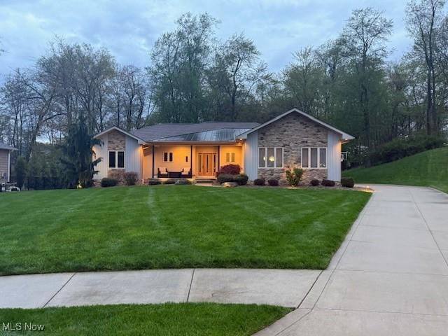 single story home featuring stone siding, a front yard, and driveway