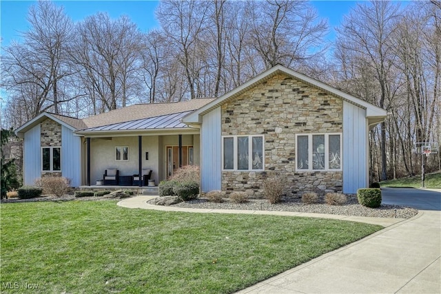 ranch-style house featuring stone siding, a standing seam roof, a front lawn, metal roof, and a porch