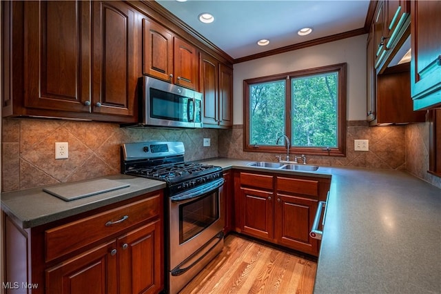 kitchen with stainless steel appliances, a sink, crown molding, decorative backsplash, and light wood finished floors