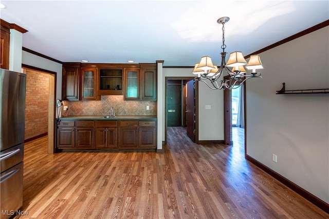kitchen with ornamental molding, a chandelier, freestanding refrigerator, light wood-type flooring, and decorative backsplash