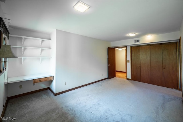 unfurnished bedroom with light carpet, baseboards, a closet, and a desk