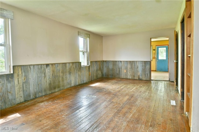 unfurnished room with wainscoting, wood-type flooring, and wooden walls