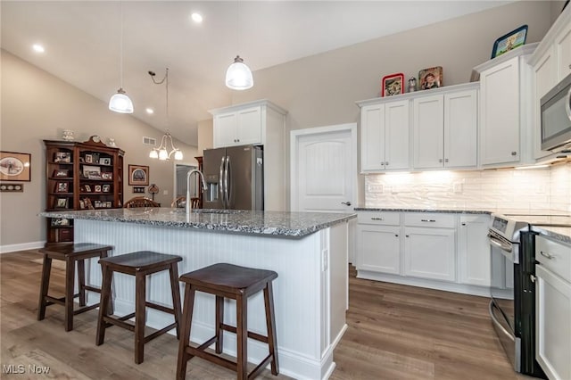 kitchen with stainless steel appliances, a sink, white cabinetry, wood finished floors, and vaulted ceiling