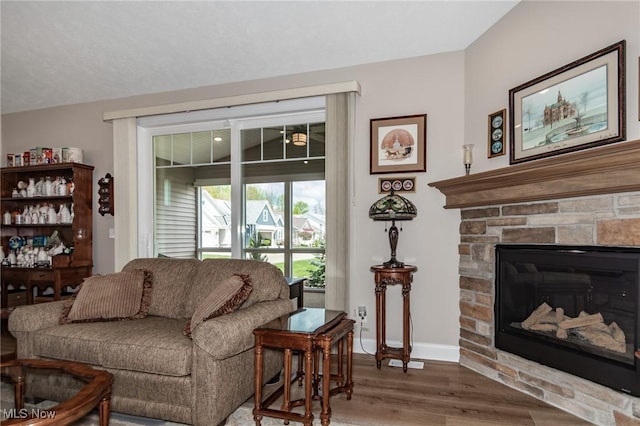 living room featuring wood finished floors, a stone fireplace, and baseboards