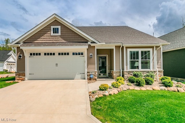 craftsman-style home with concrete driveway, stone siding, a garage, a front yard, and roof with shingles