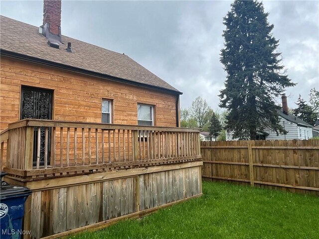 rear view of house featuring roof with shingles, a wooden deck, and fence