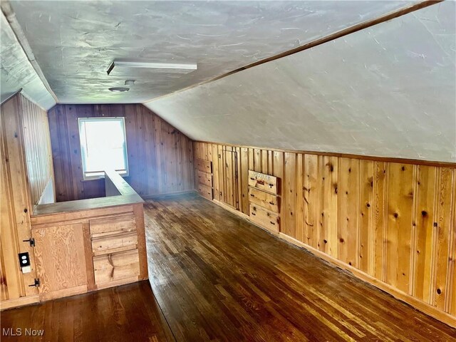 bonus room featuring dark wood-type flooring, vaulted ceiling, and wood walls