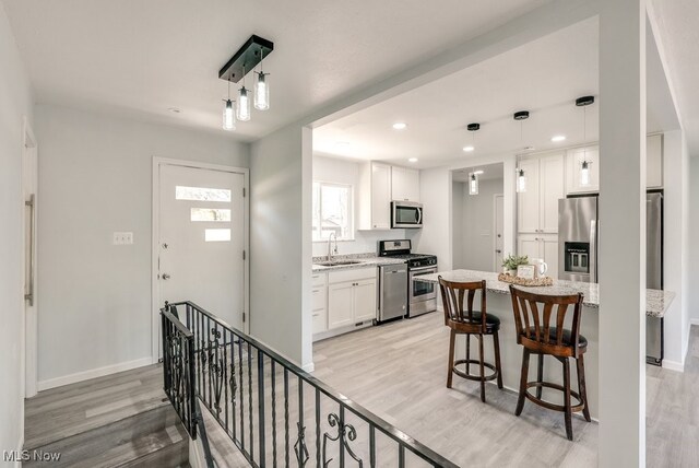 kitchen featuring stainless steel appliances, a sink, light wood finished floors, white cabinetry, and recessed lighting