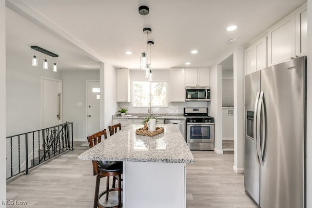 kitchen featuring appliances with stainless steel finishes, baseboards, light wood finished floors, white cabinetry, and light stone countertops