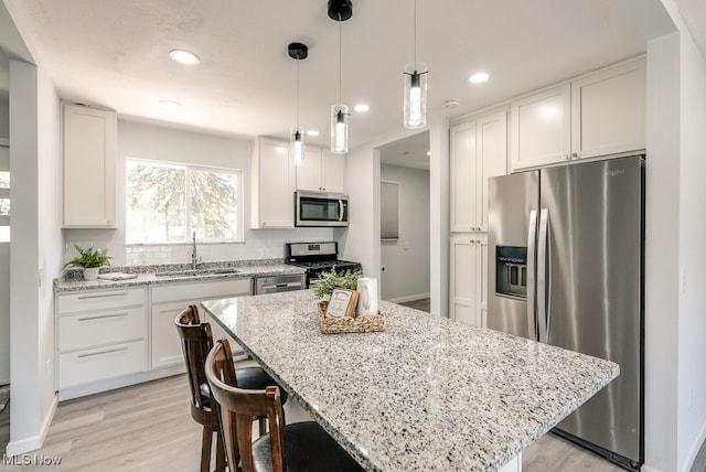 kitchen with stainless steel appliances, a sink, white cabinets, a kitchen island, and light wood-style flooring