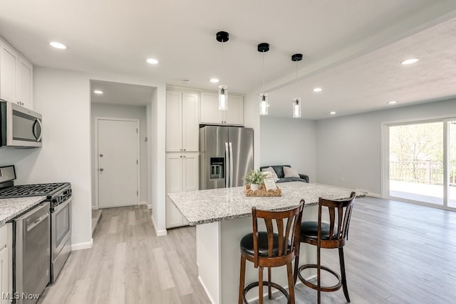 kitchen with appliances with stainless steel finishes, light wood-style flooring, a kitchen bar, light stone countertops, and white cabinetry