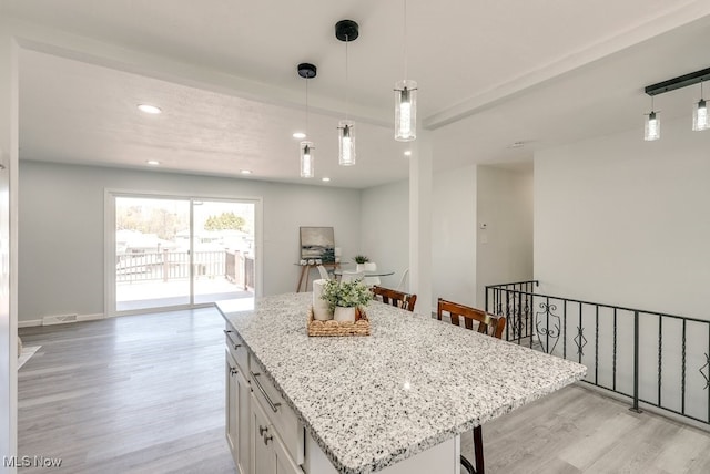 kitchen with a kitchen breakfast bar, light wood-type flooring, light stone counters, white cabinets, and a center island