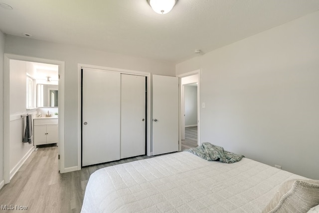 bedroom with light wood-style floors, a closet, baseboards, a sink, and connected bathroom