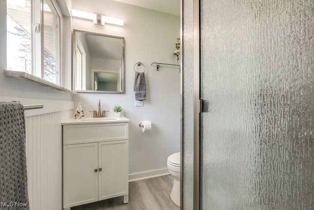 bathroom featuring wood finished floors, toilet, vanity, a stall shower, and baseboards