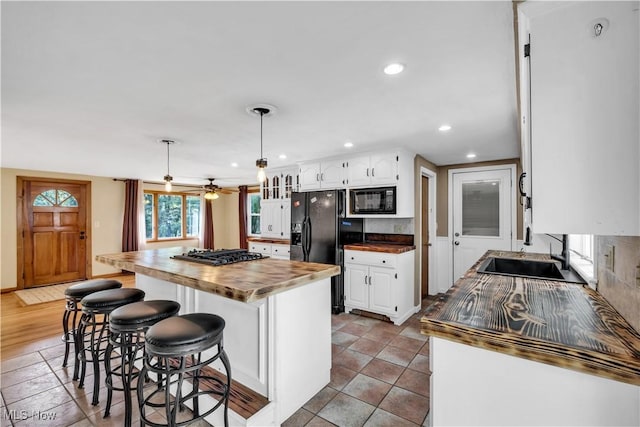 kitchen with black appliances, butcher block countertops, white cabinets, a center island, and a breakfast bar area