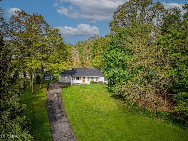 view of front of house with asphalt driveway, a front yard, and a forest view