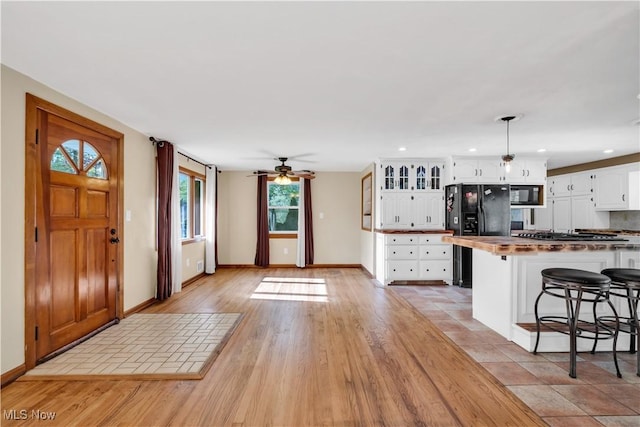 kitchen with black appliances, white cabinetry, baseboards, a breakfast bar, and a ceiling fan