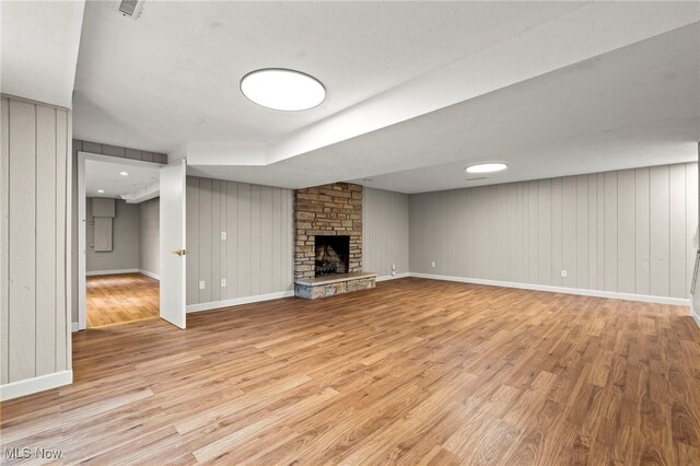 unfurnished living room featuring light wood-type flooring, a fireplace, baseboards, and wooden walls