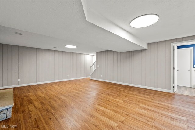 finished below grade area featuring wood finished floors, baseboards, stairway, and wooden walls