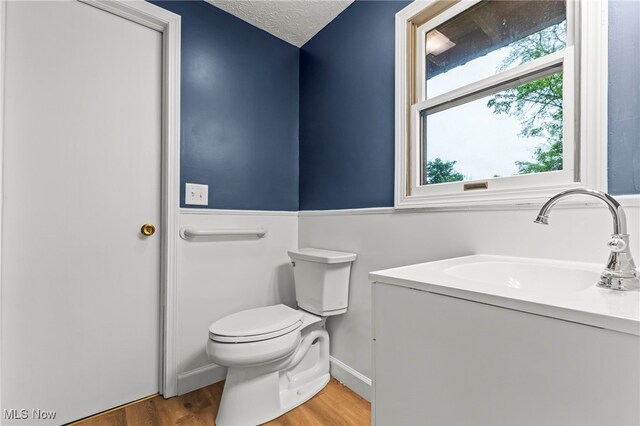 bathroom with toilet, wood finished floors, a textured ceiling, baseboards, and a sink