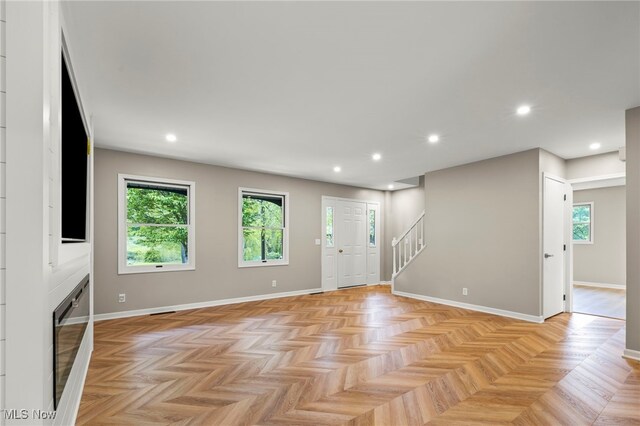 unfurnished living room with stairway, plenty of natural light, recessed lighting, and baseboards