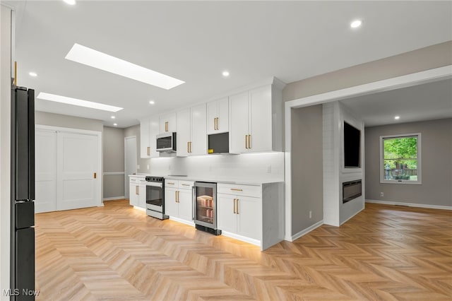 kitchen featuring beverage cooler, electric stove, stainless steel microwave, white cabinetry, and light countertops