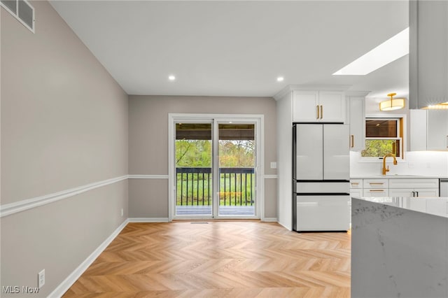 kitchen with refrigerator, a skylight, white cabinets, baseboards, and recessed lighting