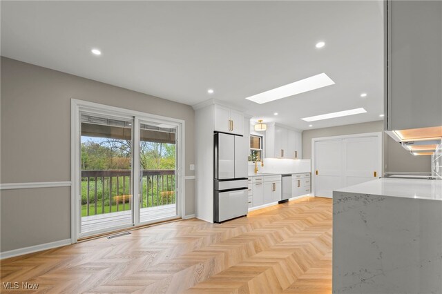 kitchen featuring freestanding refrigerator, dishwasher, a skylight, white cabinets, and light countertops