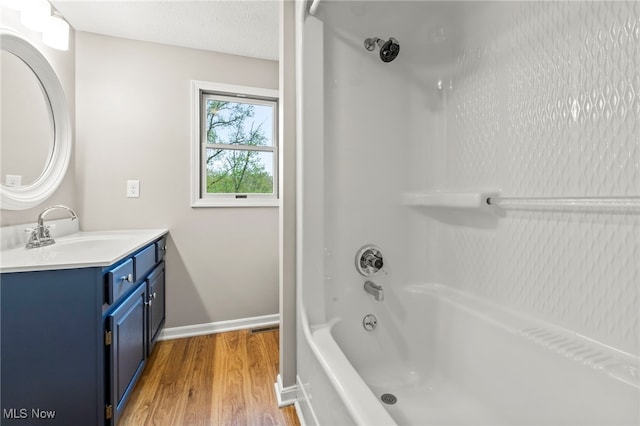 full bath featuring wood finished floors, baseboards, vanity, and tub / shower combination