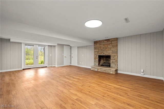unfurnished living room with light wood-style flooring, a fireplace, baseboards, and wood walls