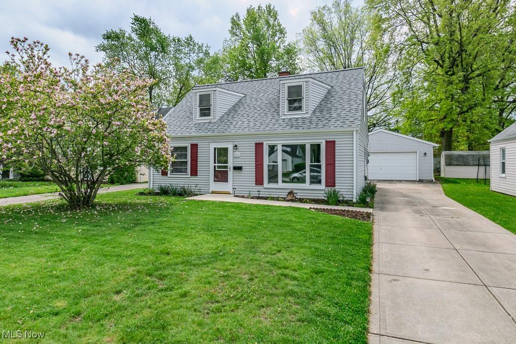 cape cod house featuring an outbuilding, a detached garage, a shingled roof, a front lawn, and a chimney