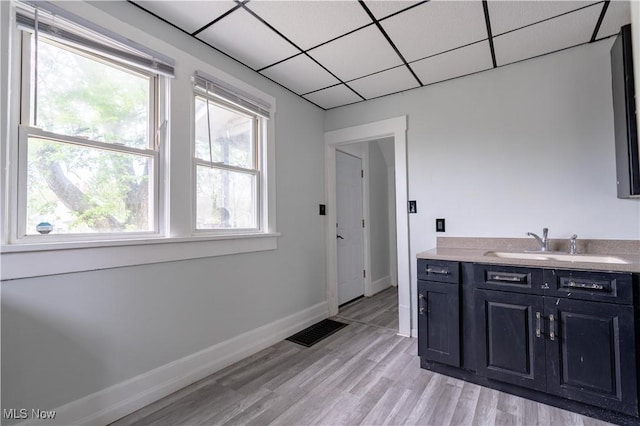 bar area featuring a sink, plenty of natural light, light wood finished floors, baseboards, and a paneled ceiling