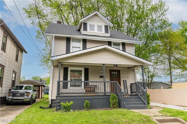 american foursquare style home with covered porch, a chimney, a front yard, and roof with shingles