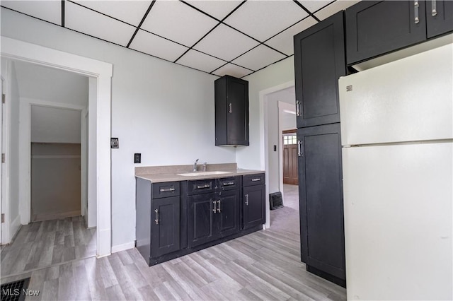 kitchen featuring freestanding refrigerator, a sink, light wood-type flooring, light countertops, and baseboards