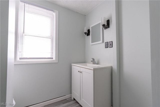 bathroom with plenty of natural light, wood finished floors, vanity, a baseboard radiator, and a textured ceiling