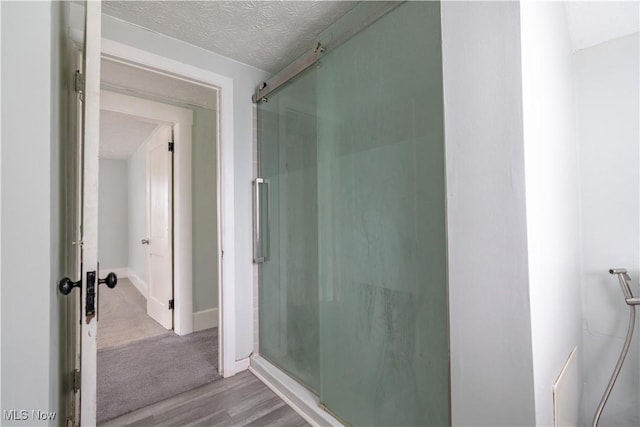 full bath featuring a stall shower, wood finished floors, baseboards, and a textured ceiling