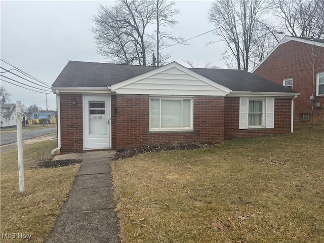 bungalow-style house with brick siding, a front yard, and a shingled roof