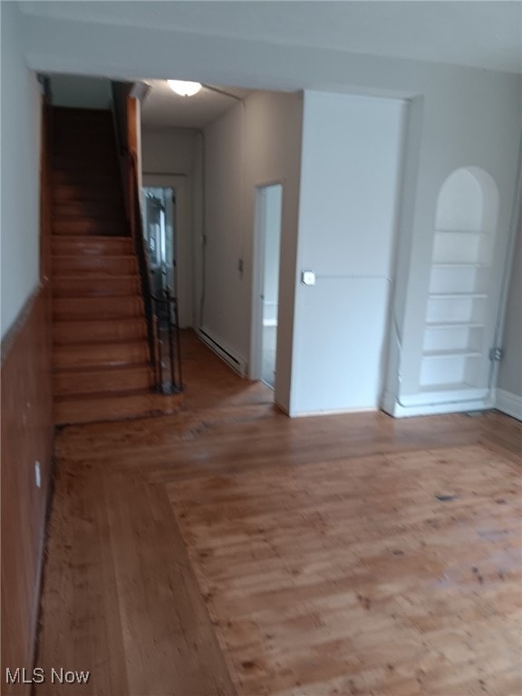 unfurnished room featuring a baseboard heating unit, wood finished floors, and stairs