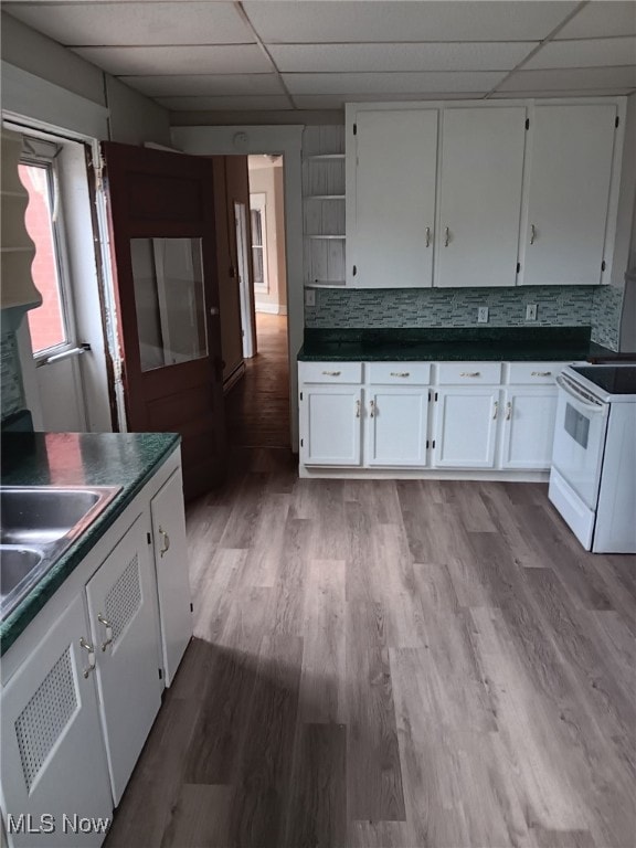 kitchen with white electric stove, a drop ceiling, dark countertops, white cabinets, and backsplash