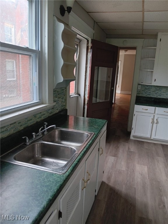 kitchen featuring a sink, wood finished floors, a paneled ceiling, white cabinetry, and dark countertops