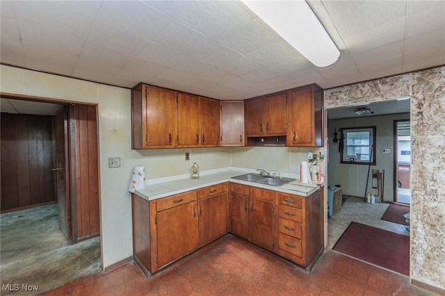 kitchen with a sink, light countertops, brown cabinetry, baseboards, and wooden walls
