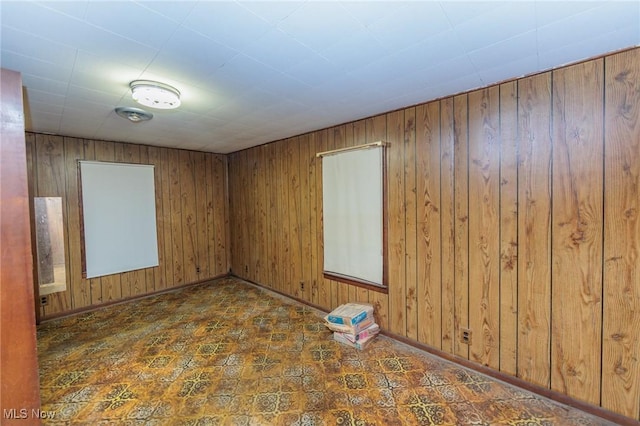 unfurnished room featuring wood walls, baseboards, and tile patterned floors