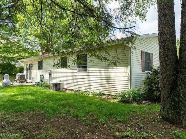 view of home's exterior with central air condition unit, a lawn, and a chimney