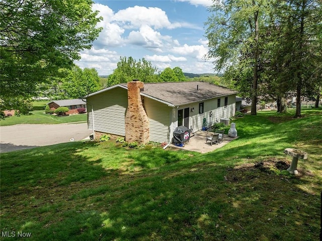 rear view of house featuring a patio area, a chimney, and a yard