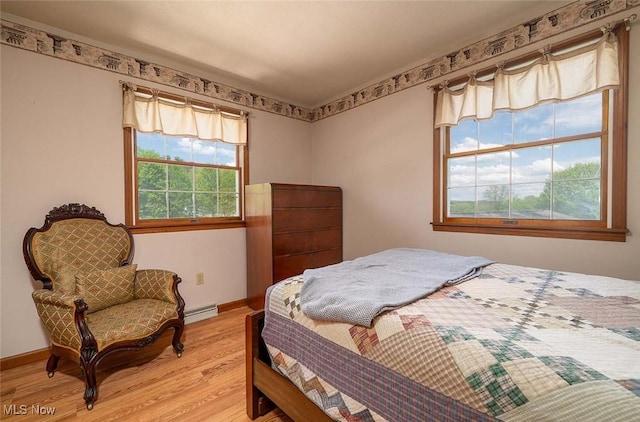 bedroom with light wood finished floors, baseboards, and a baseboard radiator
