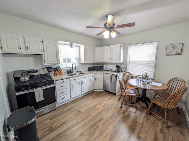 kitchen featuring stainless steel appliances, a sink, white cabinets, light wood finished floors, and ceiling fan